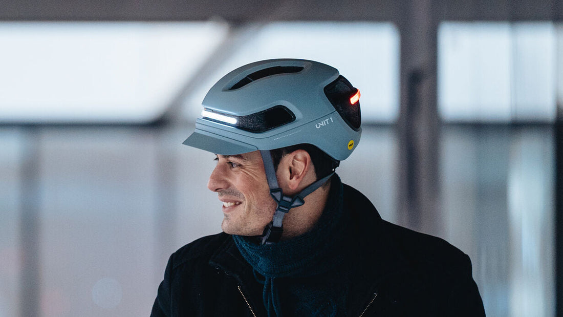 Un adulte circulant en trottinette électrique et portant un casque connecté "UNIT 1" dans une rue de la ville