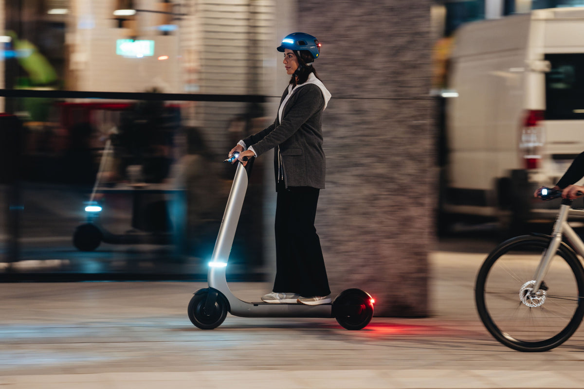 Adult rider on an electric scooter wearing a UNIT 1 smart helmet on a city street