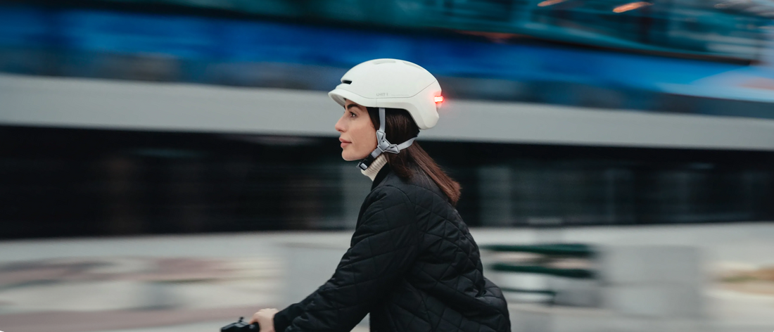 Un adulte circulant en trottinette électrique et portant un casque connecté "UNIT 1" dans une rue de la ville