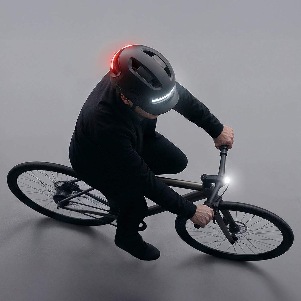 Cycliste penché sur son guidon, feux avant et arrière du casque AURA allumés